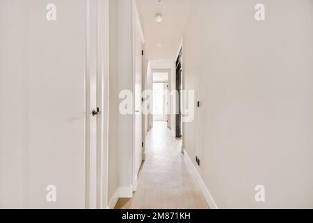 Ein langer Flur mit weißen Wänden und Holzfußboden auf jeder Seite, der zu den anderen Zimmern führt Stockfoto