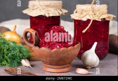 Hausgemachter würziger Kaviar aus Rüben, Karotten, Zwiebeln und Knoblauch in Schüssel und Gläsern sowie frische Zutaten auf braunem Tisch Stockfoto