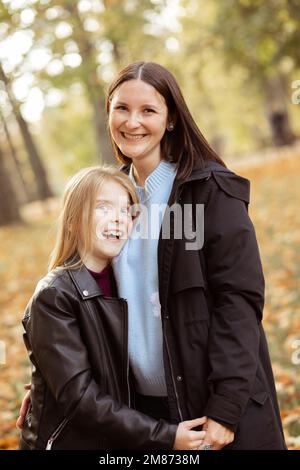 Aufrechte, fröhliche, lachende Familie von Mutter und kleiner Tochter, die umarmt, in die Kamera schaut, sich umarmt Stockfoto