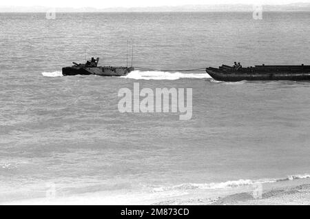 Ein AAV-7-Amphibienfahrzeug der Kompanie A, 2. Assault Amphibian Bataillon, schleppt einen Abschnitt der Brücke hinaus ins Meer, wo es mit anderen Abschnitten verbunden wird, um während einer Überbrückungsübung vor Kin Blue Beach eine Fähre zu bilden. Marines von Co B, 9. Engineer Support BN., 3. Force Service Support GRP., nehmen ebenfalls an der Übung Teil. Staat: Okinawa Land: Japan (JPN) Stockfoto