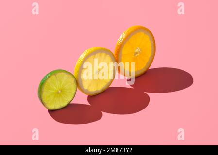 Scheiben Limette, Zitrone und Orange auf einem rosafarbenen Tisch in hellem Licht. Scheiben verschiedener Zitrusfrüchte minimalistisch auf einem lebendigen Hintergrund Stockfoto