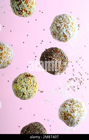 Schwebende verschiedene vegane Süßigkeiten, köstliche Bonbons mit Samen, getrocknete Früchte, gesunde Süßigkeiten mit Chia, Sesamsamen und Kokosnuss auf rosa Backgrou Stockfoto