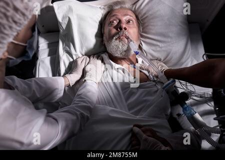 Kranke ältere Mann wachte auf der Intensivstation, in Schock und Angst. Draufsicht, nach der Operation. Team von Krankenschwestern und Ärzten helfen bei der Pflege von kranken Senior m Stockfoto