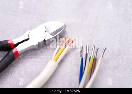 Elektrokabel ohne Isolierung und Drahtschneider auf einem grauen Tisch. Stockfoto