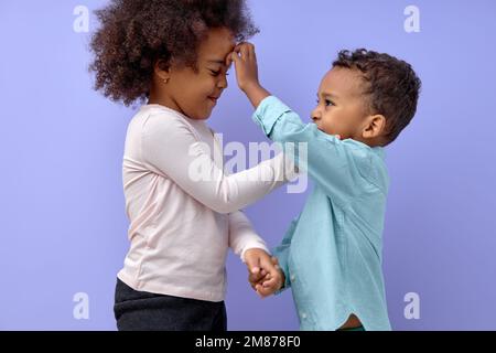 Aufgeregter Bruder und Schwester haben Spaß zusammen, sie posieren vor der Kamera isoliert im lila Studiohintergrund. Porträt fröhlich lächelnder Kinder in zwangloser c Stockfoto