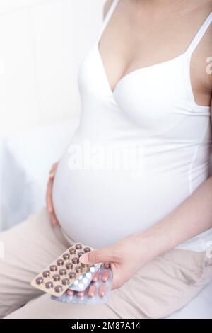 Schwangere Frauen saßen auf dem Bett und hielten Pillen Stockfoto