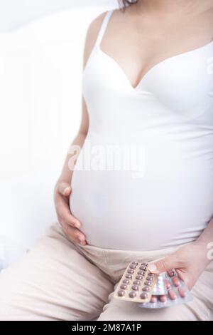 Schwangere Frauen saßen auf dem Bett und hielten Pillen Stockfoto