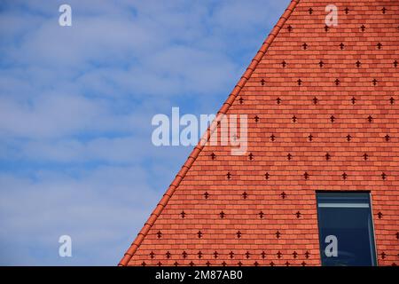 Tonziegeldach mit steilem Hang in rotbrauner Farbe. Dachfenster oder Oberlicht. Metalleis und Schneeschutz in quadratischem Muster. Schneebrecher. Baugewerbe. Stockfoto