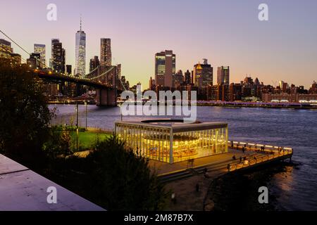 Blick in die Dämmerung auf Jane's Carousel mit der East River Brooklyn Bridge und der Skyline des Lower Manhattan Financial District im Hintergrund von Brooklyn Bridge Park.Brooklyn.New York City.USA Stockfoto