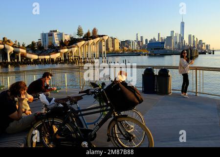 Besucher entspannen sich am Pier 57 mit Little Island am Hudson River und der Skyline des Lower Manhattan Financial District im Hintergrund.Manhattan.New York City.USA Stockfoto