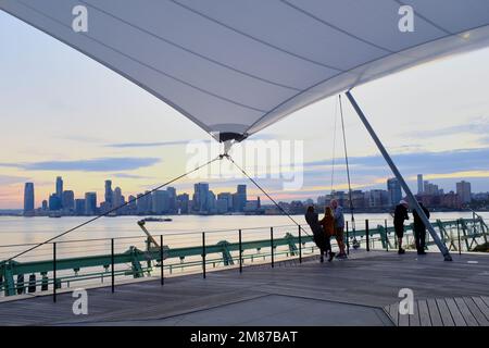 Besucher im Pier 57 Rooftop Park mit Hudson River und Jersey City Skyline im Hintergrund nach Sonnenuntergang.Manhattan.New York City.USA Stockfoto