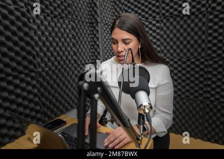 Frau, die in ein Mikrofon in einer Audiokabine spricht, während sie einen Podcast aufnimmt. Stockfoto