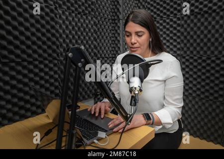 Frau, die in ein Mikrofon in einer Audiokabine spricht, während sie einen Podcast aufnimmt. Stockfoto