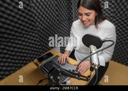 Draufsicht einer Frau, die einen Podcast in einer Audiokabine aufnimmt. Stockfoto