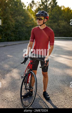 Ein gutaussehender Mann mit sportlicher Körperform, Schutzhelm und Brille, der sich beim Fahrradfahren mit schöner Natur ausruhen kann. Sportbegriff, Stockfoto