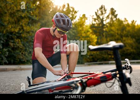 Ein Typ, der Halt hat, draußen ist, Fahrrad durch eigene Kräfte repariert, sich ändernde Details, Probleme mit Bewegung, ein weißer Sportler, der sportlich wirkt Stockfoto