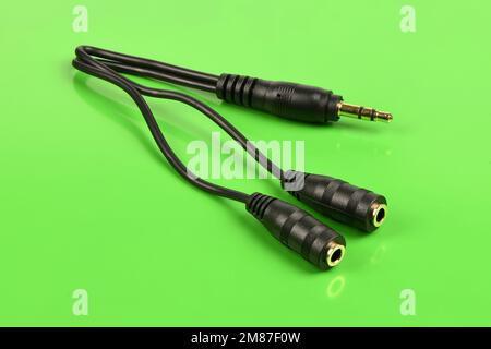 Audiokabel-Splitter, Stereo-Stecker auf zwei Stereo-Audio-Buchsen 3,5 mm, isoliert auf grünem Hintergrund. Extreme Nahaufnahme. Hochauflösendes Foto. Voll Stockfoto