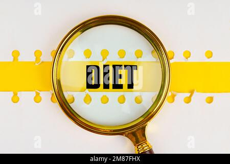 Zwischen zwei Blättern aus einem Notizbuch auf einem gelben Streifen mit der Aufschrift „Diet“ befindet sich eine Lupe. Stockfoto