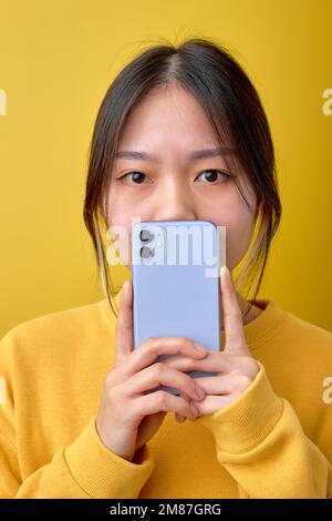 Nahaufnahme eines schockierten asiatischen Mädchens, das Smartphone in den Händen hält, Nachrichten liest, mit großen Augen in die Kamera schaut, denkt, was ich sagen soll, Surpr Stockfoto