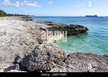 Der malerische Blick auf die erodierte felsige Küste der Insel Grand Bahama und ein Industrieschiff, das im Wet Dock festgemacht ist. Stockfoto