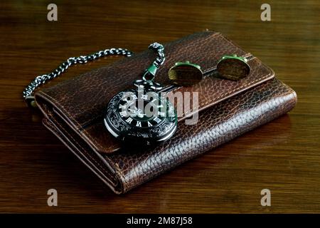 Ledertasche mit schwarzer Taschenuhr und goldenen Manschettenknöpfen auf polierter Holzoberfläche Stockfoto