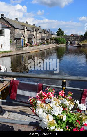 Eine terrassenförmige Reihe hübscher Hütten entlang des Kanalbeckens des Monmouthshire Brecon Canal. Blaue Türen und attraktive Blumen vor dem Hotel. Stockfoto