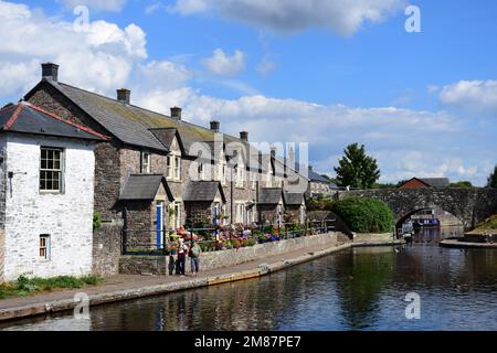 Eine terrassenförmige Reihe hübscher Hütten entlang des Kanalbeckens des Monmouthshire Brecon Canal. Blaue Türen und attraktive Blumen vor dem Hotel Stockfoto