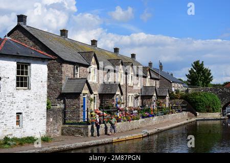 Eine terrassenförmige Reihe hübscher Hütten entlang des Kanalbeckens des Monmouthshire Brecon Canal. Blaue Türen und attraktive Blumen vor dem Hotel Stockfoto