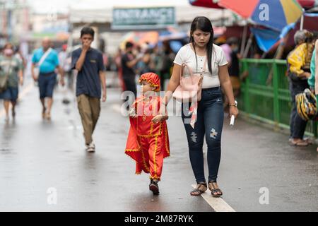 Ein kleines Kind in einem santo Nino Outfit geht mit seiner Mutter während des jährlichen Sinulog Festivals in Cebu City, Philippinen, die Straße entlang Stockfoto