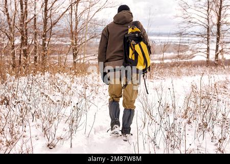 Rückansicht eines unbekannten Mannes, der mit einem Rucksack reist. Winterwanderung im Wald. Tourist auf Wanderung im Winter im Wald, Natur. buschboot, Jagd, Trav Stockfoto