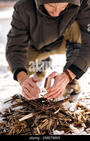 Nahaufnahmen von Männchen, die im Wald ein Feuer entfachen. Ein Feuer in der Natur durch einen Mann anzünden. Feuer aus Holz. Ruhiger, einsamer Mann in warmer Kleidung in Natu Stockfoto