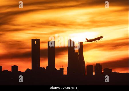 Madrid, Spanien. 12. Januar 2023. Nach dem Abflug vom Flughafen Adolfo Suarez Madrid Barajas bei Sonnenuntergang ist die Sonne ein Flugzeug, das über die Wolkenkratzer von Madrids Skyline, auch bekannt als „Four Towers Business Area“, fliegt. Kredit: Marcos del Mazo/Alamy Live News Stockfoto