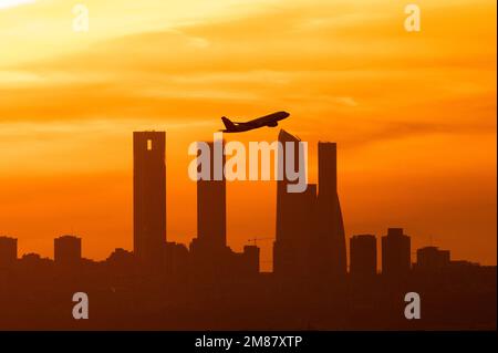 Madrid, Spanien. 12. Januar 2023. Nach dem Abflug vom Flughafen Adolfo Suarez Madrid Barajas bei Sonnenuntergang ist die Sonne ein Flugzeug, das über die Wolkenkratzer von Madrids Skyline, auch bekannt als „Four Towers Business Area“, fliegt. Kredit: Marcos del Mazo/Alamy Live News Stockfoto