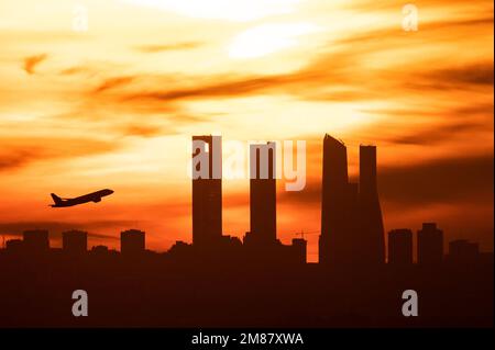 Madrid, Spanien. 12. Januar 2023. Nach dem Abflug vom Flughafen Adolfo Suarez Madrid Barajas bei Sonnenuntergang ist die Sonne ein Flugzeug, das über die Wolkenkratzer von Madrids Skyline, auch bekannt als „Four Towers Business Area“, fliegt. Kredit: Marcos del Mazo/Alamy Live News Stockfoto