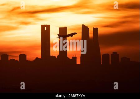 Madrid, Spanien. 12. Januar 2023. Nach dem Abflug vom Flughafen Adolfo Suarez Madrid Barajas bei Sonnenuntergang ist die Sonne ein Flugzeug, das über die Wolkenkratzer von Madrids Skyline, auch bekannt als „Four Towers Business Area“, fliegt. Kredit: Marcos del Mazo/Alamy Live News Stockfoto