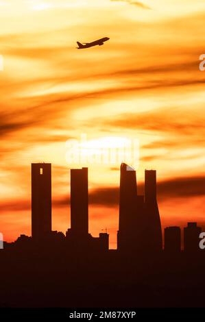 Madrid, Spanien. 12. Januar 2023. Nach dem Abflug vom Flughafen Adolfo Suarez Madrid Barajas bei Sonnenuntergang ist die Sonne ein Flugzeug, das über die Wolkenkratzer von Madrids Skyline, auch bekannt als „Four Towers Business Area“, fliegt. Kredit: Marcos del Mazo/Alamy Live News Stockfoto