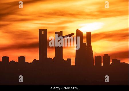 Madrid, Spanien. 12. Januar 2023. Nach dem Abflug vom Flughafen Adolfo Suarez Madrid Barajas bei Sonnenuntergang ist die Sonne ein Flugzeug, das über die Wolkenkratzer von Madrids Skyline, auch bekannt als „Four Towers Business Area“, fliegt. Kredit: Marcos del Mazo/Alamy Live News Stockfoto