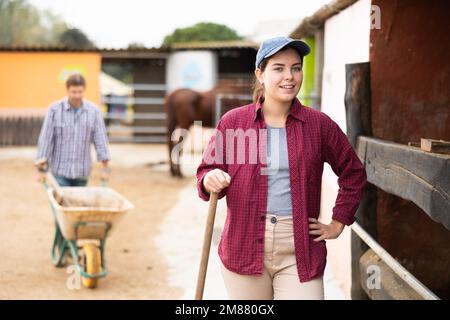 Porträt einer lächelnden jungen Bauernfrau im Garten des Bauernhofs beim Putzen Stockfoto