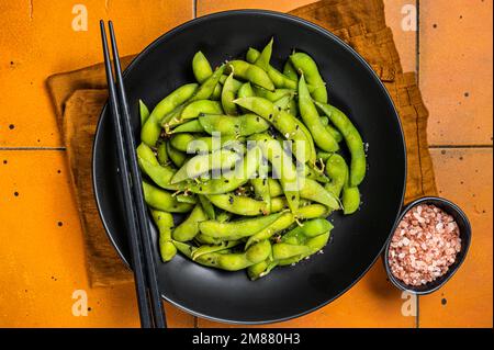 Gekochte Edamam-Sojabohnen mit Meersalz und Sesamsamen. Orangefarbener Hintergrund. Draufsicht. Stockfoto