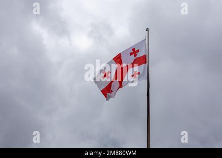 Georgische Nationalflagge (Fünffarge), die vor dem ehemaligen georgischen Parlamentsgebäude in Kutaisi im Wind vor bewölktem Himmel winkt. Stockfoto