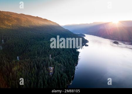 Drohnenfoto vom Sonnenaufgang über den Bergen und Meeresaufnahme von Quarry Rock mit Wanderer auf dem Gipfel in Deep Cove, North Vancouver. Stockfoto
