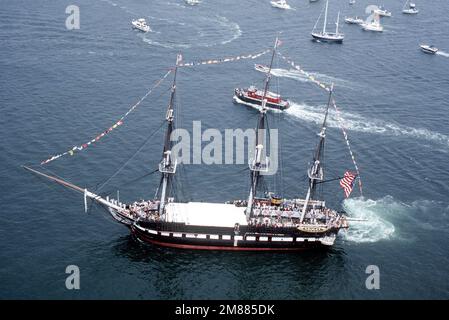 Ein Luftblick auf die 44-Pistolen-Segelfregatte USS CONSTITUTION, die während der jährlichen Rundfahrt im Hafen von einem Feuerschlepper unterstützt wird. Nach dem Abfeuern eines 21-Pistolen-Salutschusses an die Nation wird das Schiff in die entgegengesetzte Richtung zum Liegeplatz zurückgebracht, um ein gleichmäßiges Wettern zu ermöglichen und das Holz zu erhalten. Basis: Boston Harbor State: Massachusetts (MA) Land: Vereinigte Staaten von Amerika (USA) Stockfoto