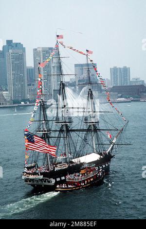 Ein Luftblick auf die 44-Pistolen-Segelfregatte USS CONSTITUTION, die während der jährlichen Rundfahrt im Hafen von einem Feuerschlepper unterstützt wird. Nach dem Abfeuern eines 21-Pistolen-Salutschusses an die Nation wird das Schiff in die entgegengesetzte Richtung zum Liegeplatz zurückgebracht, um ein gleichmäßiges Wettern zu ermöglichen und das Holz zu erhalten. Basis: Boston Harbor State: Massachusetts (MA) Land: Vereinigte Staaten von Amerika (USA) Stockfoto