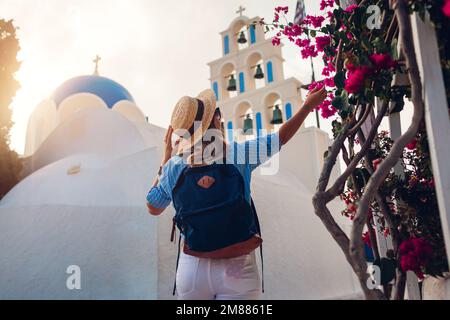 Santorin Tourist mit Rucksackwanderungen durch die Kirche mit blauer Kuppel und blühenden Bougainvillea-Blumen in Akrotiri Stockfoto