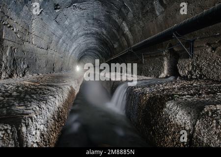 Unterirdischer, gewölbter städtischer Abwassertunnel mit schmutzigem Abwasser. Stockfoto