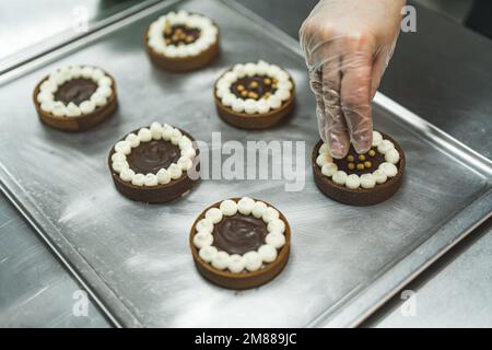 Nahaufnahme einer Bäckerhand, die den Schokoladenkuchen in der Bäckerei goldene Streusel hinzufügt. Hochwertiges Foto Stockfoto
