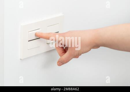 Nahaufnahme einer Frau, die das Licht mit einem Wandschalter anmacht Stockfoto