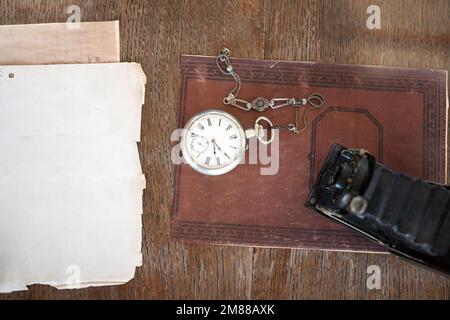 Blick von oben auf eine alte Kamera und eine alte Taschenuhr auf einem alten Buch und Schreibtisch Stockfoto