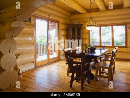 Esstisch aus Zedernholz und Stühle mit hoher Rückenlehne im Speisesaal im Blockhaus im skandinavischen Stil, Stockfoto