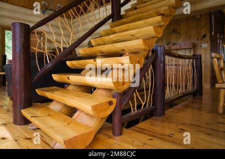 Treppen aus weißem Kiefernholz mit Zedernholzgeländern, die zum oberen Stockwerk in einem Blockhaus im skandinavischen Stil führen. Stockfoto